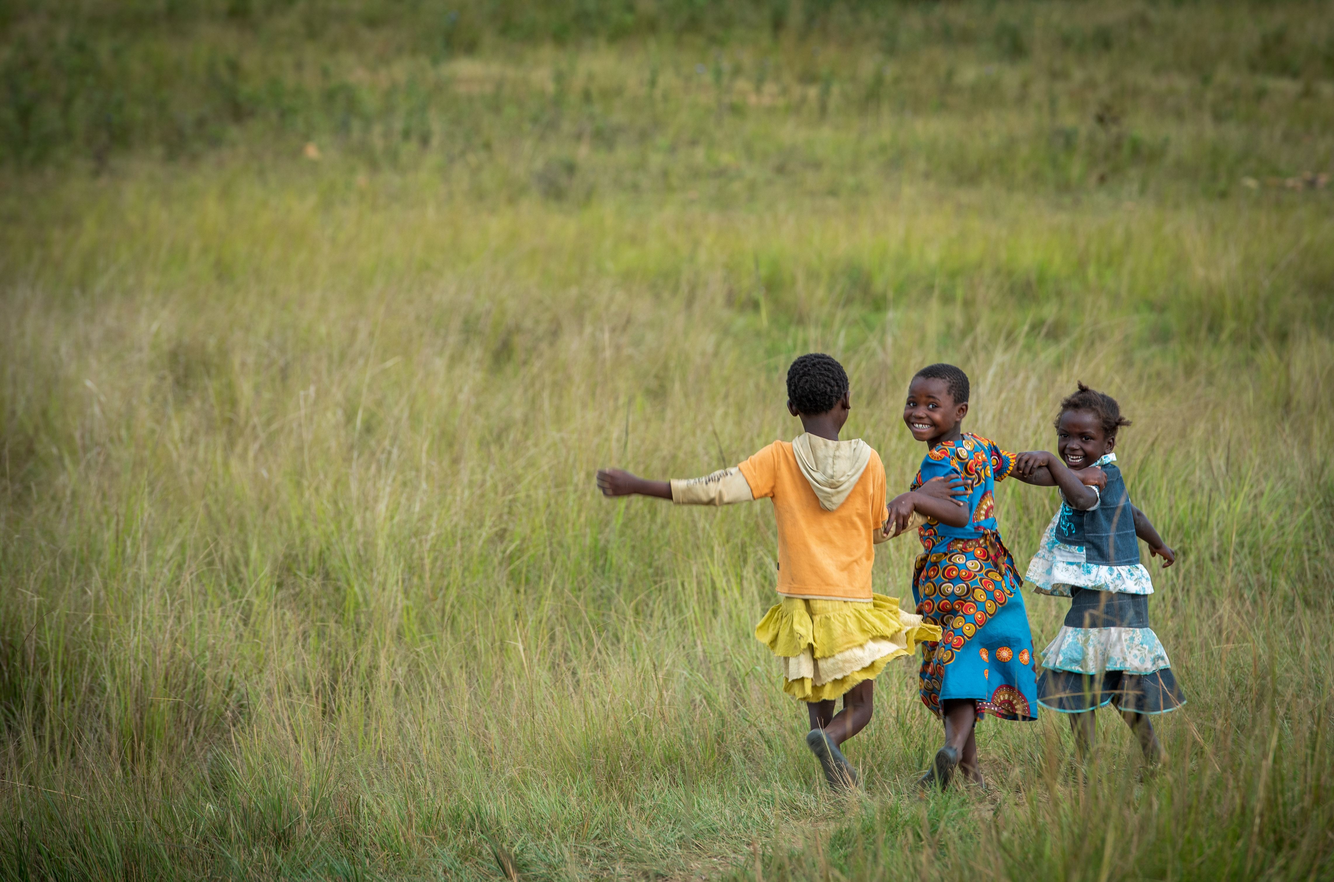 Tre bambini corrono felici attraverso un campo in Zambia