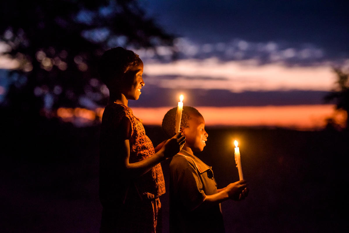 Due bambini in Zambia sorridono tenendo delle candele, sullo sfondo un tramonto