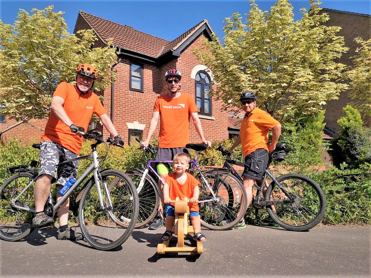 Famiglia di quattro persone posa con le biciclette in maglietta arancione per raccogliere fondi per proteggere i bambini dal coronavirus