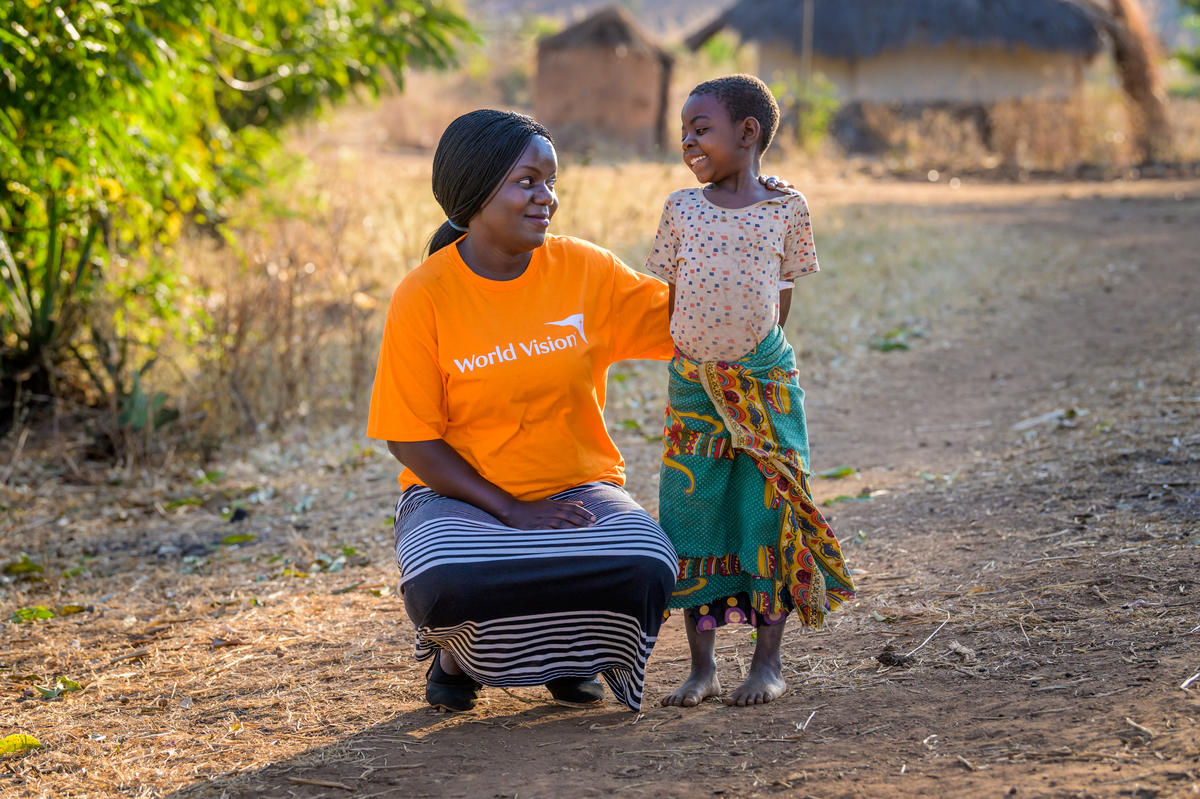 L'operatore per lo sviluppo della comunità di World Vision con una maglietta arancione si accovaccia e sorride e una ragazza che le sorride in Malawi