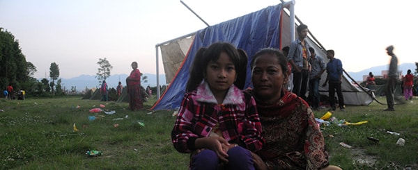 Una donna e una bambina sedute davanti a una tenda in un campo per sfollati dopo un terremoto