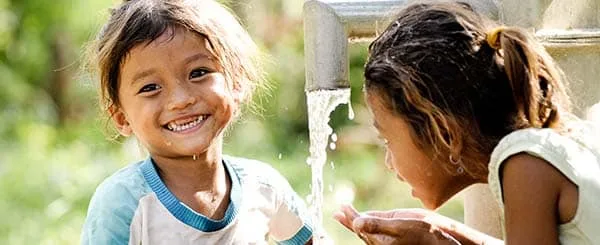 Due bambine piccole all'aperto, a fianco di un rubinetto di acqua
