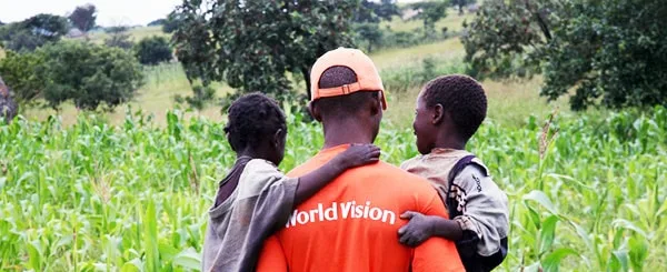 Operatore world vision che tiene in braccio due piccoli bambini in un contesto rurale