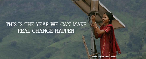 Donna sorridente in piedi accanto a un pannello solare con il testo "This is the year we can make real change happen"