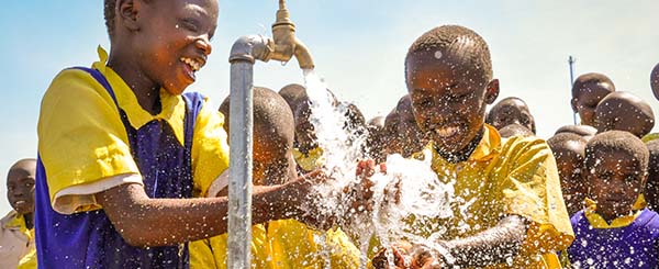 Bambini africani, vestiti con uniforme scolastica, che giocano all'aperto attorno ad un rubinetto di acqua
