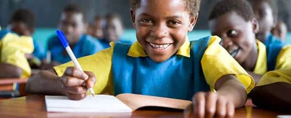 Bambino sorridente in aula scolastica mentre scrive con impegno nel suo quaderno