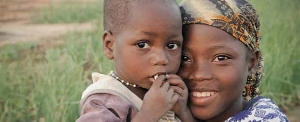 Bambino più grande sorride mentre tiene tra le braccia un bambino più piccolo in un contesto rurale