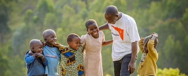 Bambini africani sorridenti assieme ad un operatore world vision, che indossa una maglietta bianca con il logo dell'organizzazione