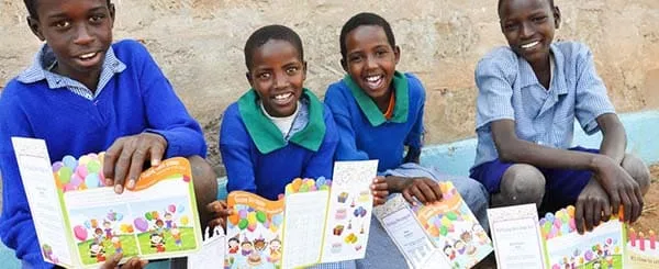Quattro bambini sorridenti mostrano libri colorati durante un'attività educativa all'aperto