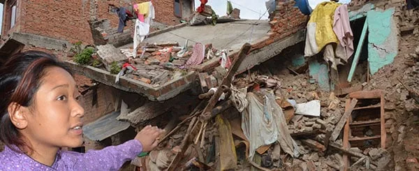 Macerie dopo il terremoto in Nepal con una donna che guarda i resti della casa