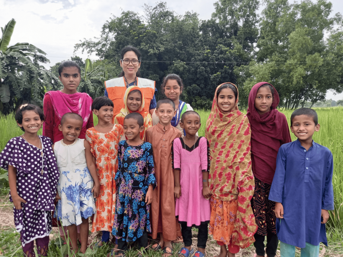 Immagine di World Vision raffigurante una comunità in Bangladesh. Mostra un gruppo di persone, tra cui donne e bambini, in un ambiente rurale. L'immagine evidenzia l'importanza dello sviluppo comunitario e del supporto alle famiglie locali per migliorare le condizioni di vita.